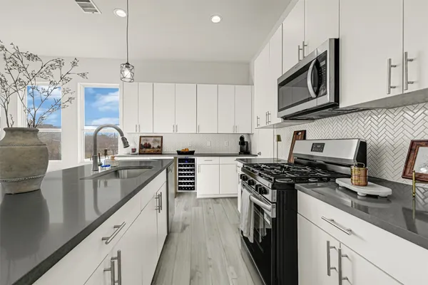 a kitchen with stainless steel appliances granite countertop a refrigerator a sink a stove a microwave and white cabinets with wooden floor