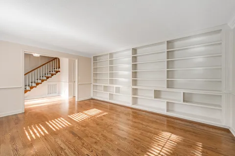 an empty room with wooden floor chandelier and windows
