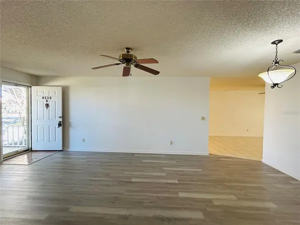a view of an empty room with wooden floor and a ceiling fan