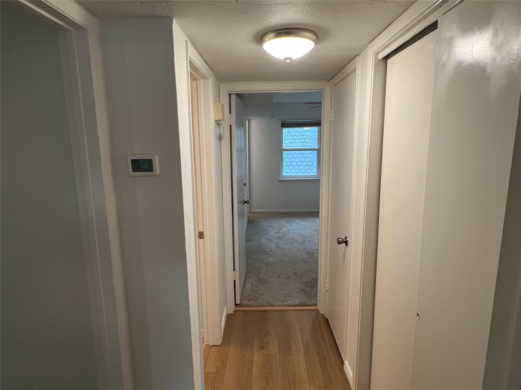 3929 Inwood Road, Unit 2021 Dallas, TX 75209 - Photo 13 of 24 Hallway featuring wood-finish flooring, flush mount lighting, a digital thermostat, and white interior doors