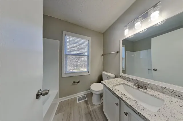 a bathroom with a granite countertop sink a toilet a mirror and a window