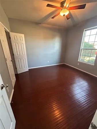 an empty room with wooden floor chandelier fan and windows