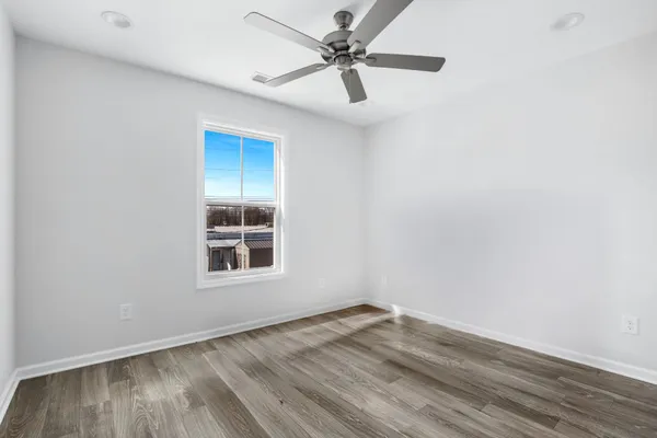 an empty room with wooden floor ceiling fan and windows