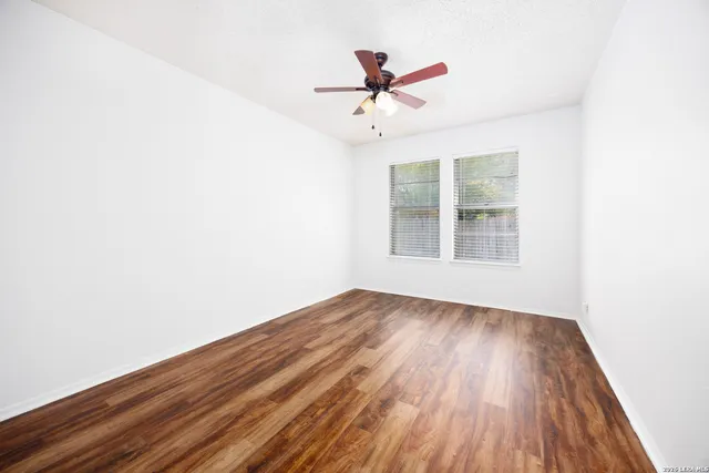 an empty room with wooden floor fan and windows