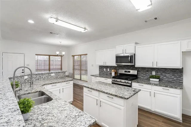 a kitchen with stainless steel appliances granite countertop a sink stove refrigerator and cabinets