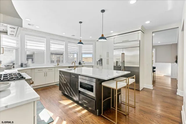 a kitchen with stainless steel appliances granite countertop a stove a sink dishwasher a refrigerator and white cabinets with wooden floor