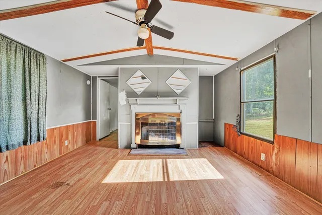 a view of an empty room with wooden floor fireplace and a window