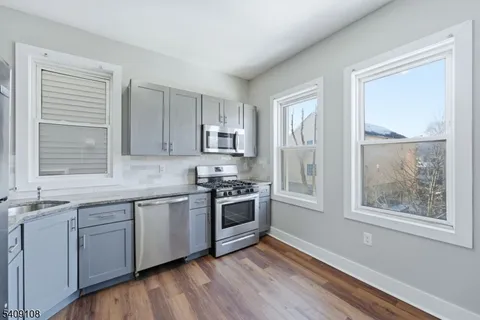 a kitchen with stainless steel appliances granite countertop a stove a sink and white cabinets with wooden floors