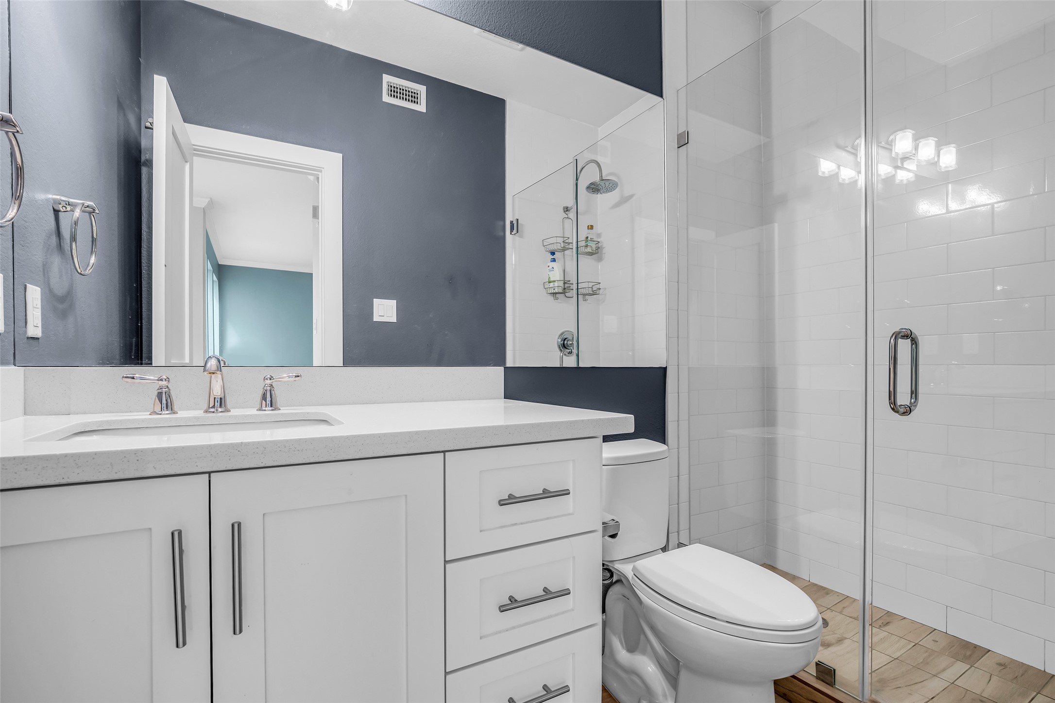 7485 Brompton Street, Unit 7485 Houston, TX 77025 - Photo 23 of 43 First floor modern bathroom with a sleek design features a stylish vanity, chrome fixtures, and ample storage. It includes a spacious glass-enclosed shower with white subway tile and a contemporary lighting.