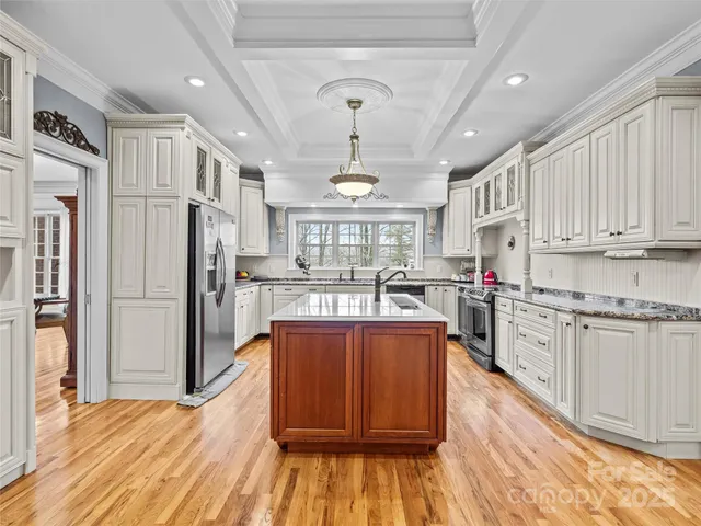 a large kitchen with stainless steel appliances granite countertop a refrigerator a stove a sink dishwasher and white cabinets with wooden floor