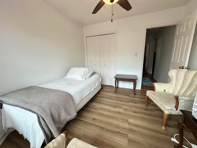 a bedroom with a bed a chair and potted plant on the dresser