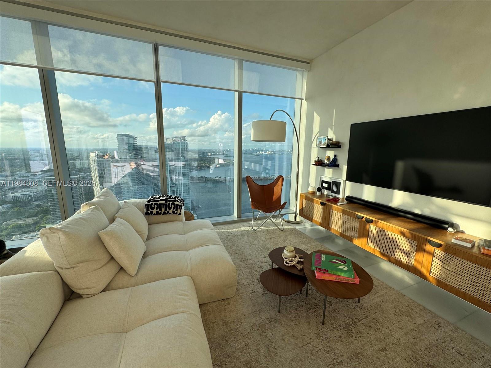 700 Northeast 26th Terrace, Unit 5006 Miami, FL 33137 - Photo 5 of 18 a living room with furniture a flat screen tv and a floor to ceiling window
