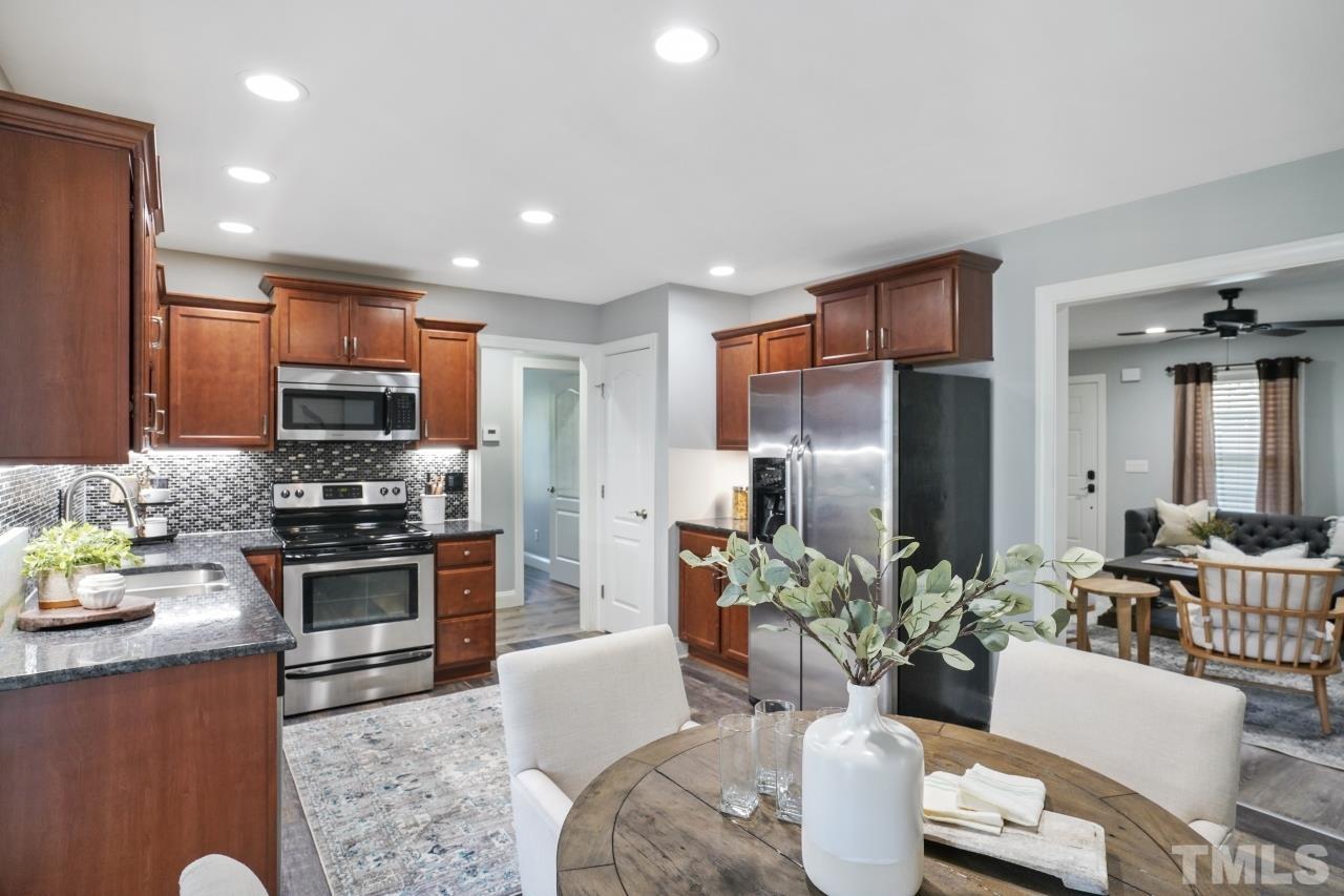 47 Hadleigh Way Fuquay-Varina, NC 27526 - Photo 9 of 37 a kitchen with stainless steel appliances granite countertop a refrigerator a stove a sink dishwasher a dining table and chairs with wooden floor