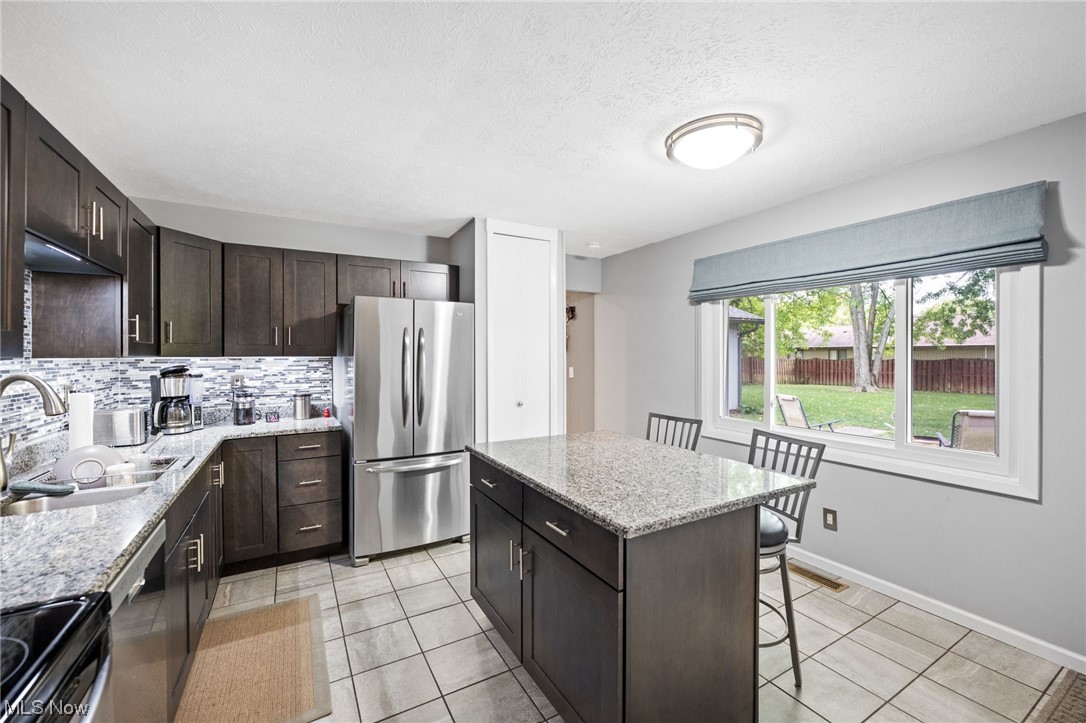 10798 Gate Post Road Strongsville, OH 44149 - Photo 17 of 32 Kitchen with light tile floors, backsplash, stainless steel refrigerator, a center island, and washbasin