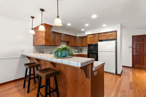 a kitchen with stainless steel appliances granite countertop a refrigerator a sink dishwasher a stove a dining table and chairs with wooden floor