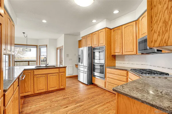 a kitchen with stainless steel appliances granite countertop a refrigerator a sink dishwasher and wooden cabinets with wooden floor