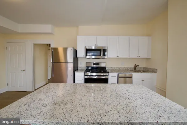 a kitchen with granite countertop a refrigerator stove top oven and sink