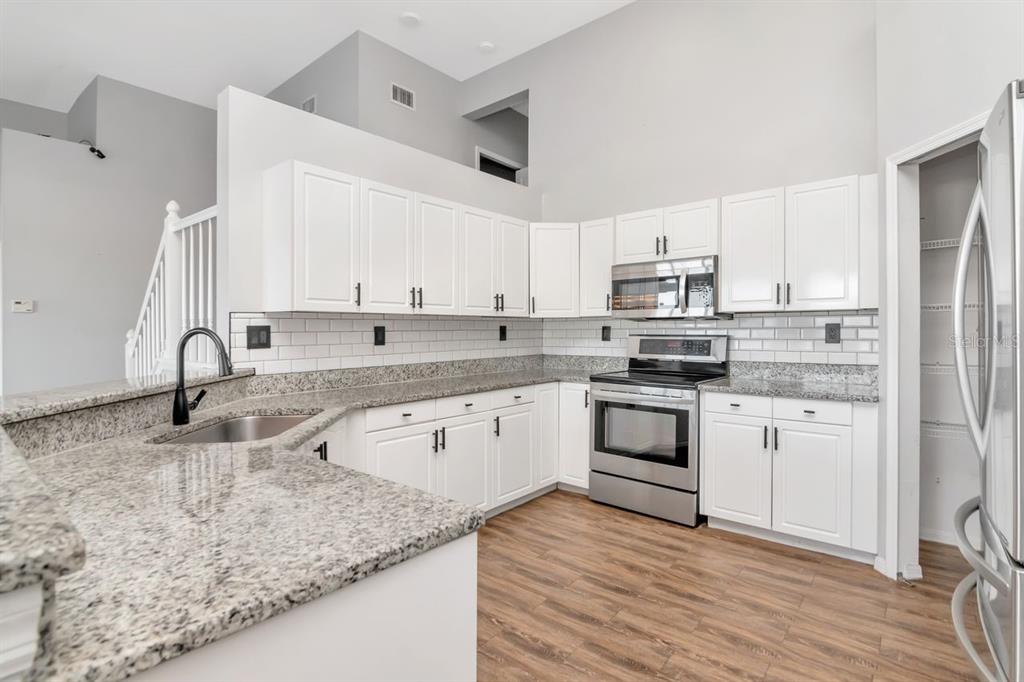 5313 Boardwalk Street Holiday, FL 34690 - Photo 29 of 69 a kitchen with stainless steel appliances granite countertop a sink dishwasher a refrigerator and white cabinets with wooden floor