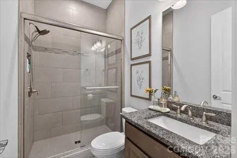 a bathroom with a granite countertop sink a mirror a shower and a toilet
