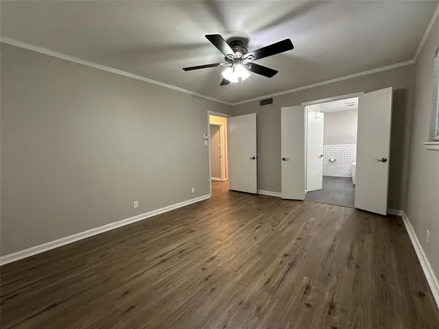 a view of an empty room with wooden floor and a ceiling fan