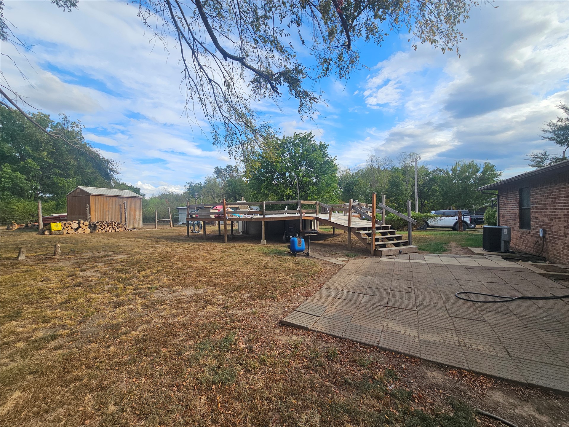 106441 South 4163rd Road Checotah, OK 74426 - Photo 13 of 17 Expansive backyard featuring a wood-sided shed, a wood-decked patio with a ramp and stairs, and a paved patio area