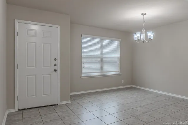 an empty room with chandelier fan and windows