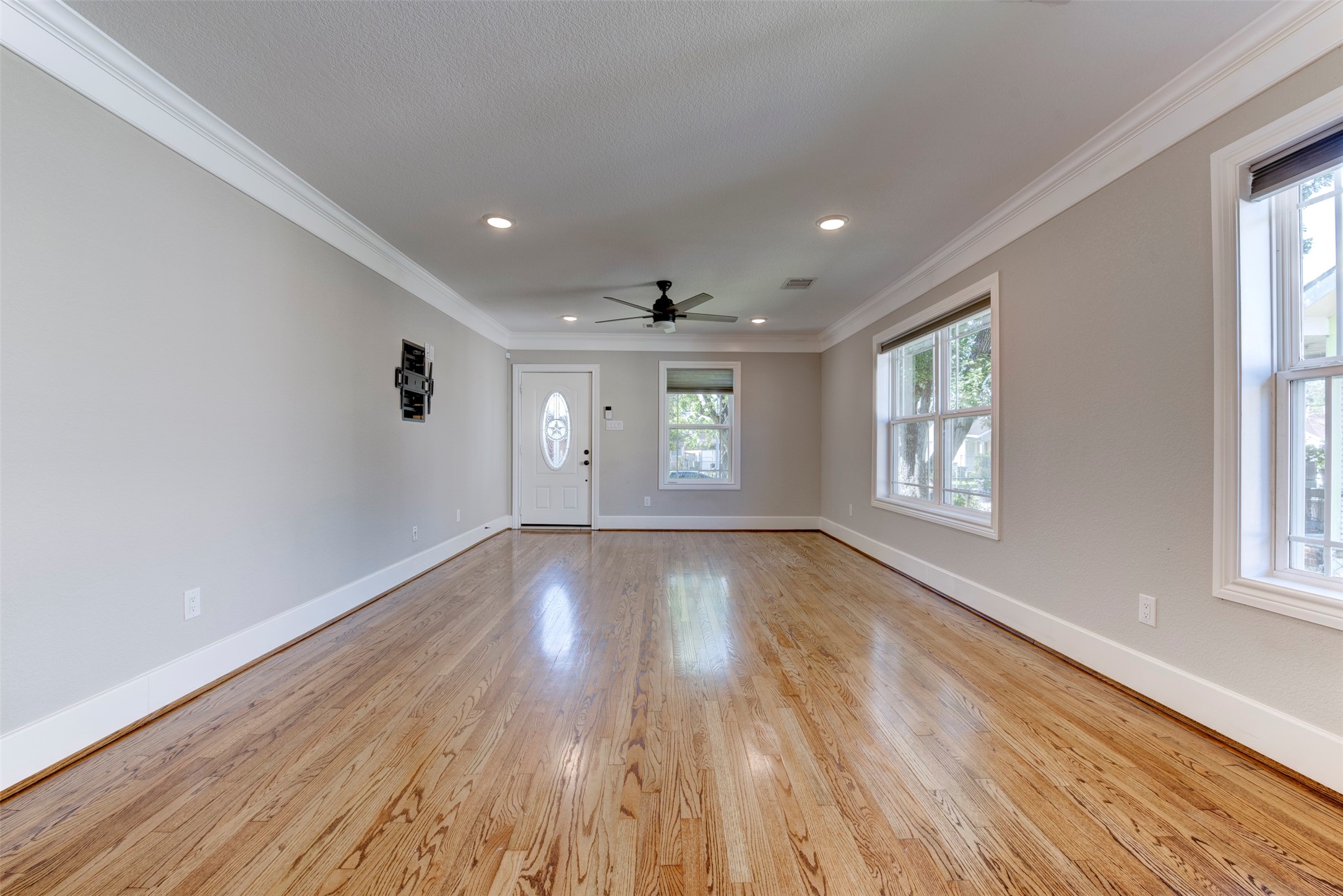 109 Dresden Street Houston, TX 77012 - Photo 8 of 43 This spacious living room features polished hardwood floors, neutral walls, recessed lighting, and ample natural light from large windows. A ceiling fan and crown molding add elegance, while the oval glass entry door enhances the space's welcoming atmosphere.