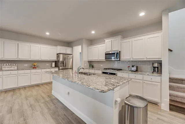 a large kitchen with stainless steel appliances granite countertop a stove a sink a refrigerator and white cabinets with wooden floor