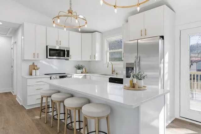 a kitchen with stainless steel appliances a sink a stove a refrigerator cabinets and chairs