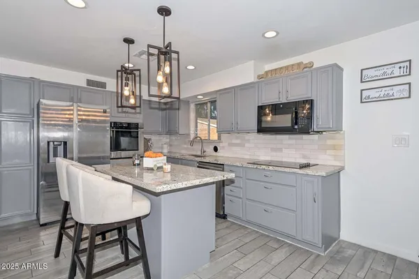 a kitchen with stainless steel appliances kitchen island granite countertop a sink a microwave refrigerator and chairs