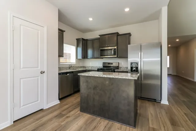 a kitchen with kitchen island granite countertop a refrigerator and a stove top oven