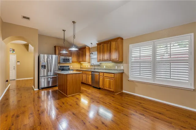 a kitchen with stainless steel appliances granite countertop a refrigerator a sink dishwasher a stove and a wooden floor