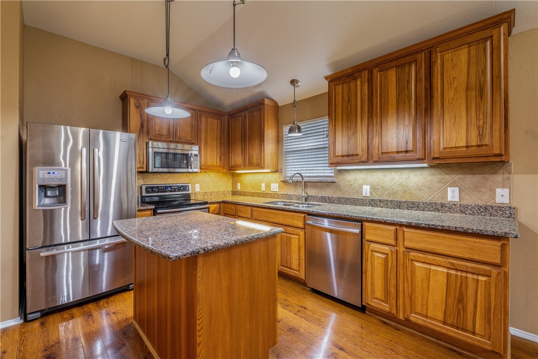 114 Inman Drive Hutto, TX 78634 - Photo 6 of 20 a kitchen with stainless steel appliances granite countertop a refrigerator a sink dishwasher and wooden cabinets with wooden floor
