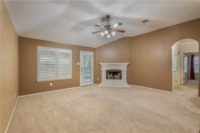 a view of an empty room with chandelier fan and fire place
