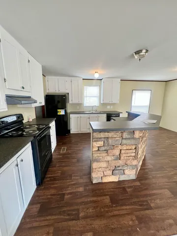 a kitchen with kitchen island granite countertop a stove top oven a sink a counter space and cabinets