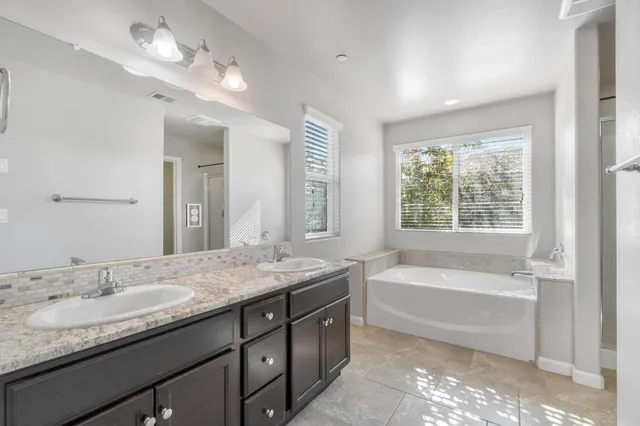 a bathroom with a granite countertop bathtub a double vanity sink and a window