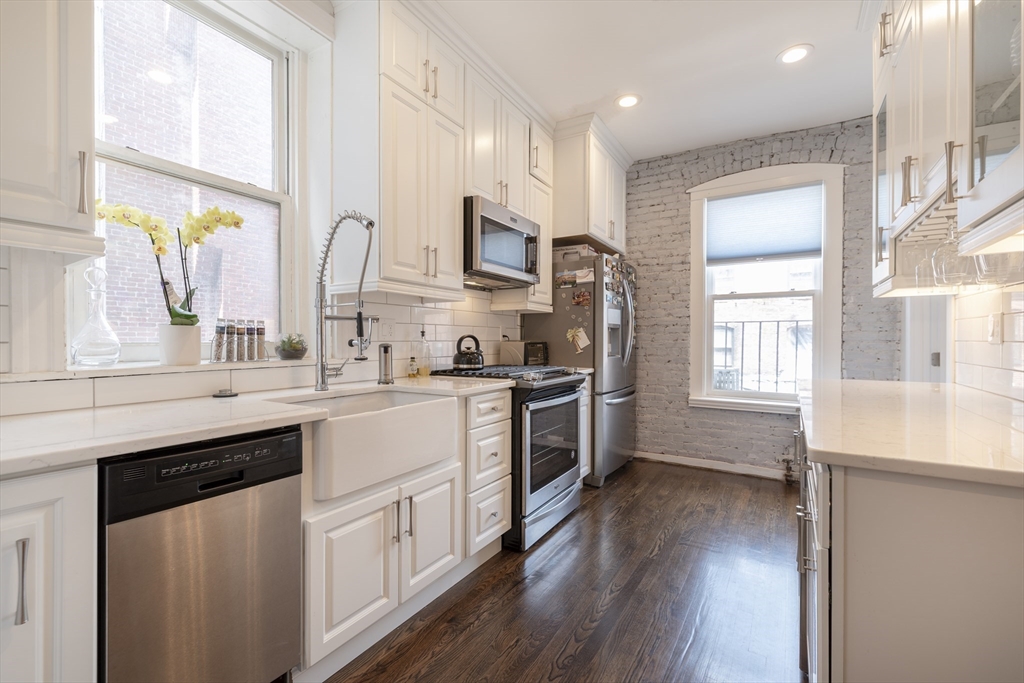 a kitchen with stainless steel appliances white cabinets a sink a window and wooden floors
