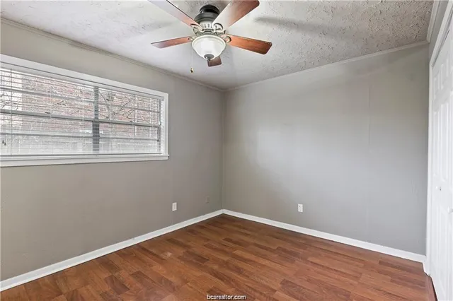 an empty room with wooden floor fan and windows