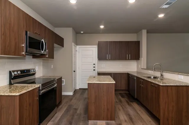 a kitchen with stainless steel appliances a sink dishwasher a stove top oven a refrigerator with wooden floor and cabinets