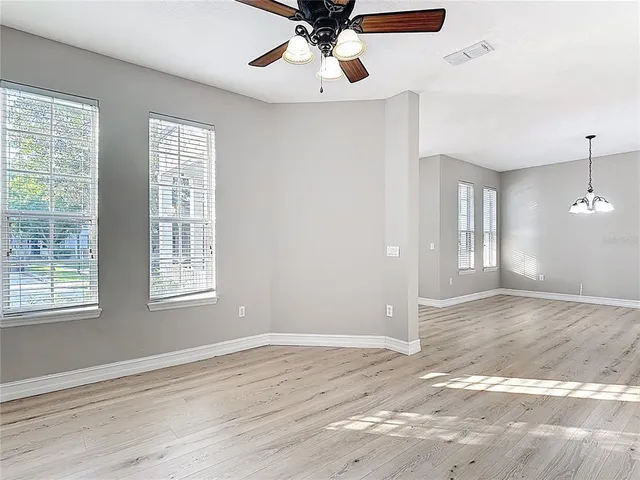 a view of an empty room with wooden floor and a ceiling fan