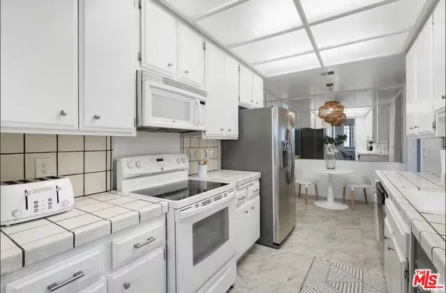 a kitchen that has a lot of white cabinets and stainless steel appliances