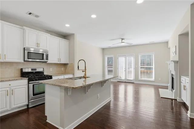 a kitchen with stainless steel appliances granite countertop a stove top oven a sink a refrigerator white cabinets and wooden floor