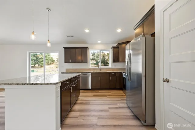 a large kitchen with stainless steel appliances kitchen island granite countertop a refrigerator and a sink