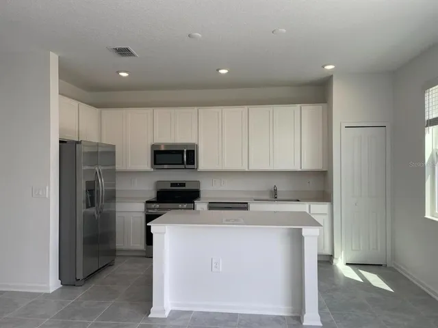 a kitchen with stainless steel appliances granite countertop a refrigerator stove a sink and white cabinets