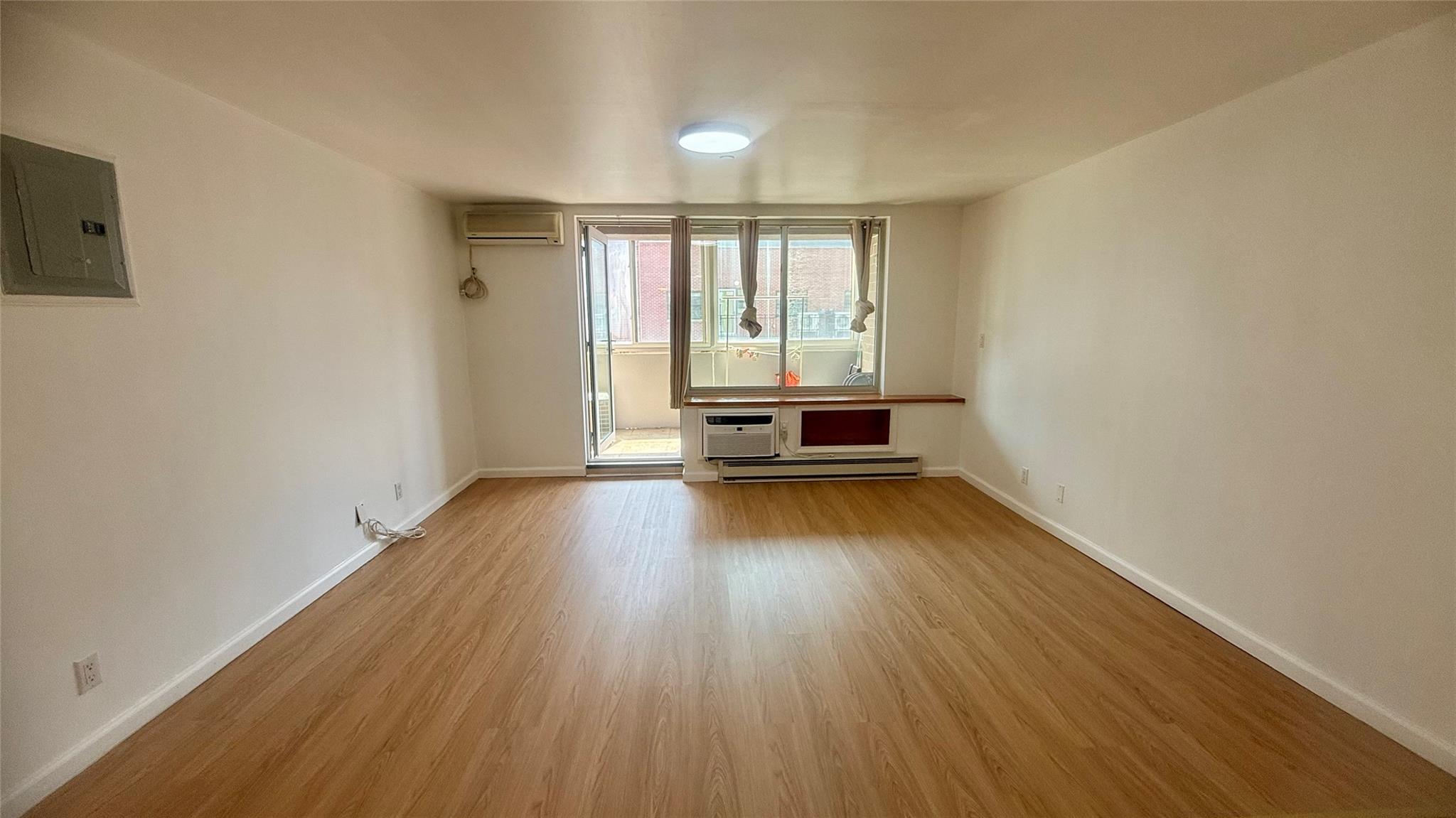 43-17 Union Street, Unit 6C Queens, NY 11355 - Photo 13 of 16 Empty room featuring a wall mounted air conditioner, baseboard heating, electric panel, wood finished floors, and an AC wall unit