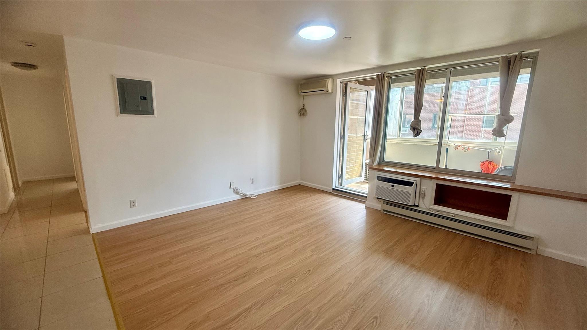 43-17 Union Street, Unit 6C Queens, NY 11355 - Photo 14 of 16 Empty room featuring a baseboard heating unit, electric panel, a wall mounted AC, light wood-type flooring, and a wall mounted air conditioner