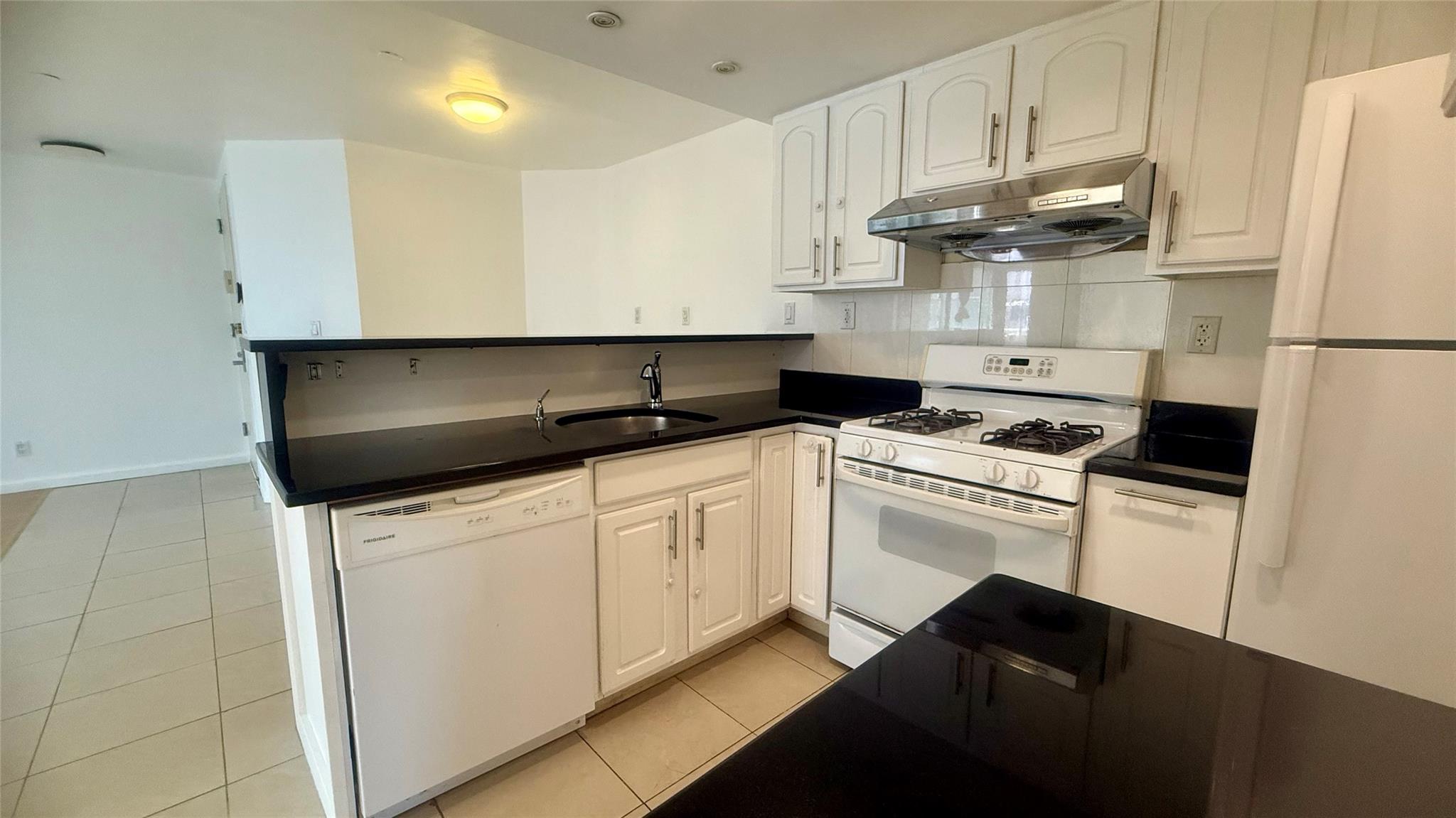 43-17 Union Street, Unit 6C Queens, NY 11355 - Photo 4 of 16 Kitchen with under cabinet range hood, white appliances, a peninsula, and dark countertops