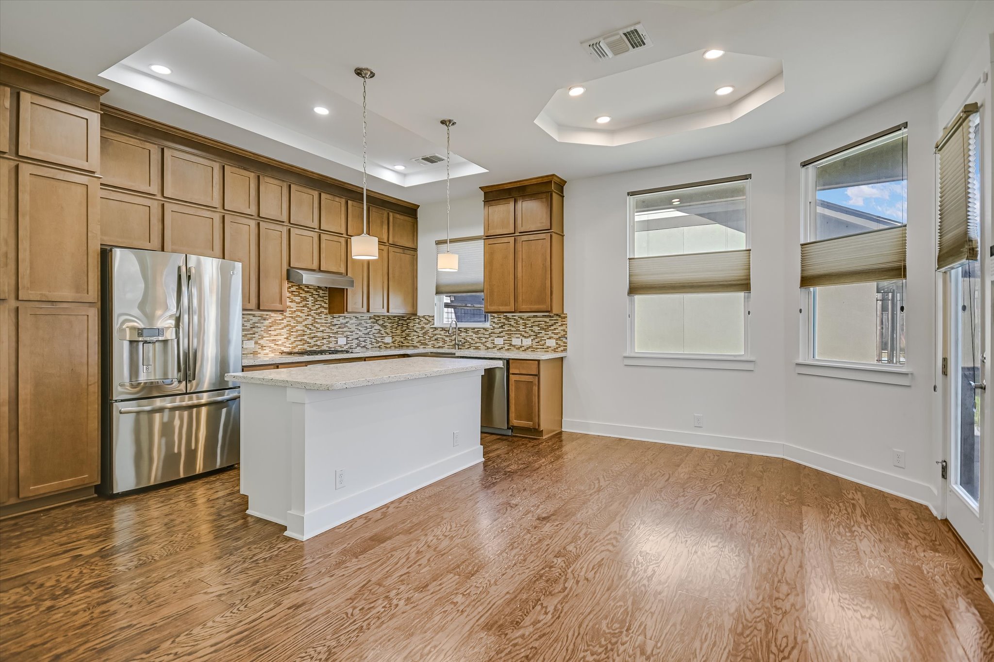 924 Sugaree Avenue Austin, TX 78757 - Photo 3 of 20 Kitchen with a tray ceiling, brown cabinets, appliances with stainless steel finishes, pendant lighting, and a kitchen island