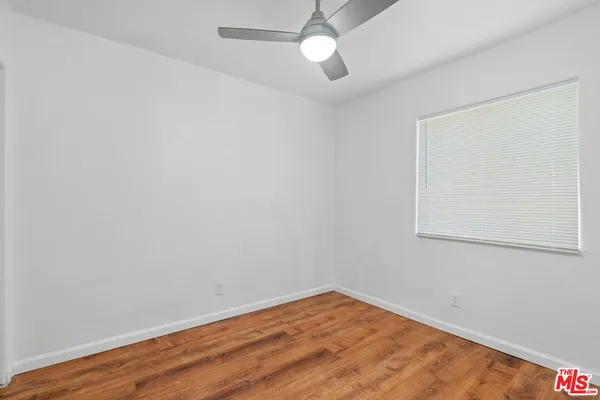 a view of an empty room with wooden floor and a ceiling fan