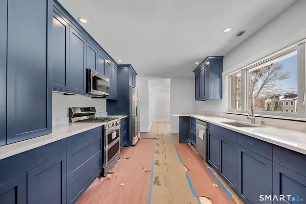 a kitchen with stainless steel appliances a sink dishwasher a stove top oven a refrigerator with wooden floors and cabinets